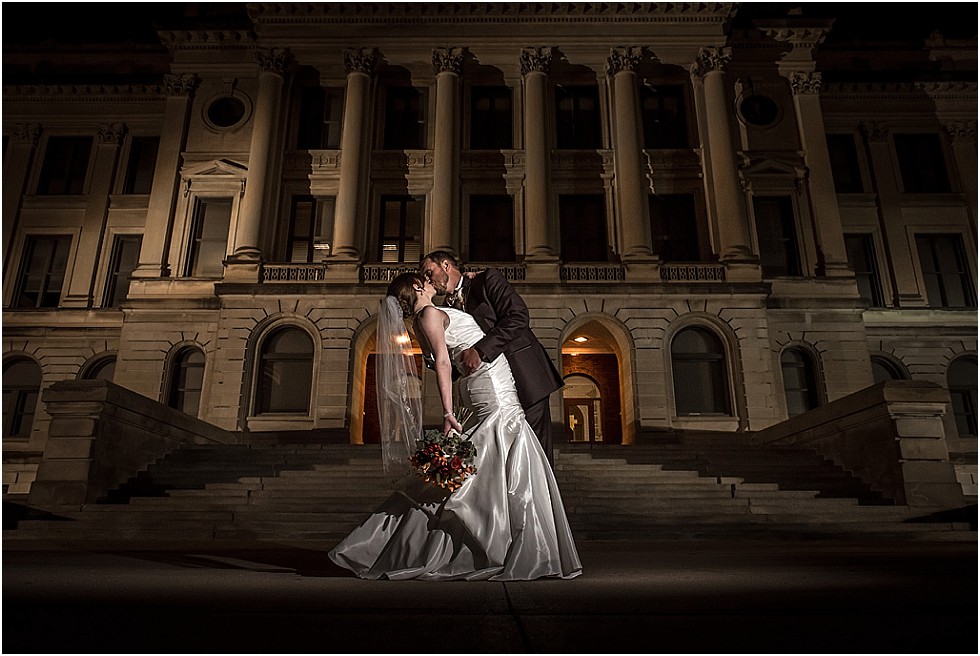 bride and groom kissing in front of Omaha Central