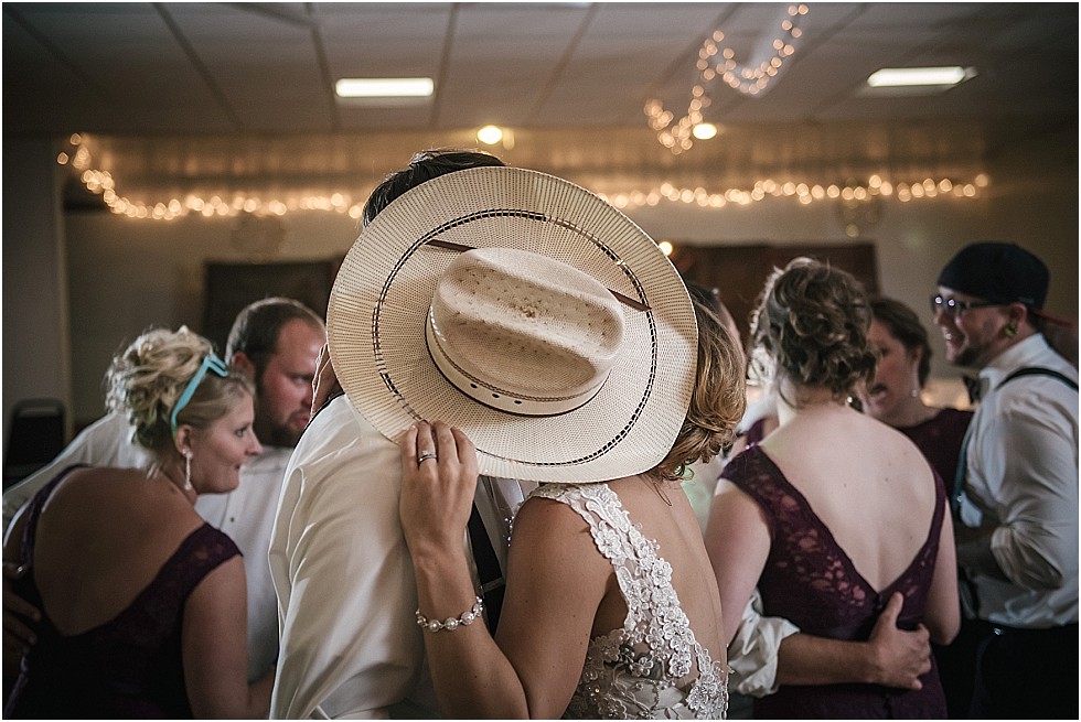 bride and groom sneak a kiss behind cowboy hat