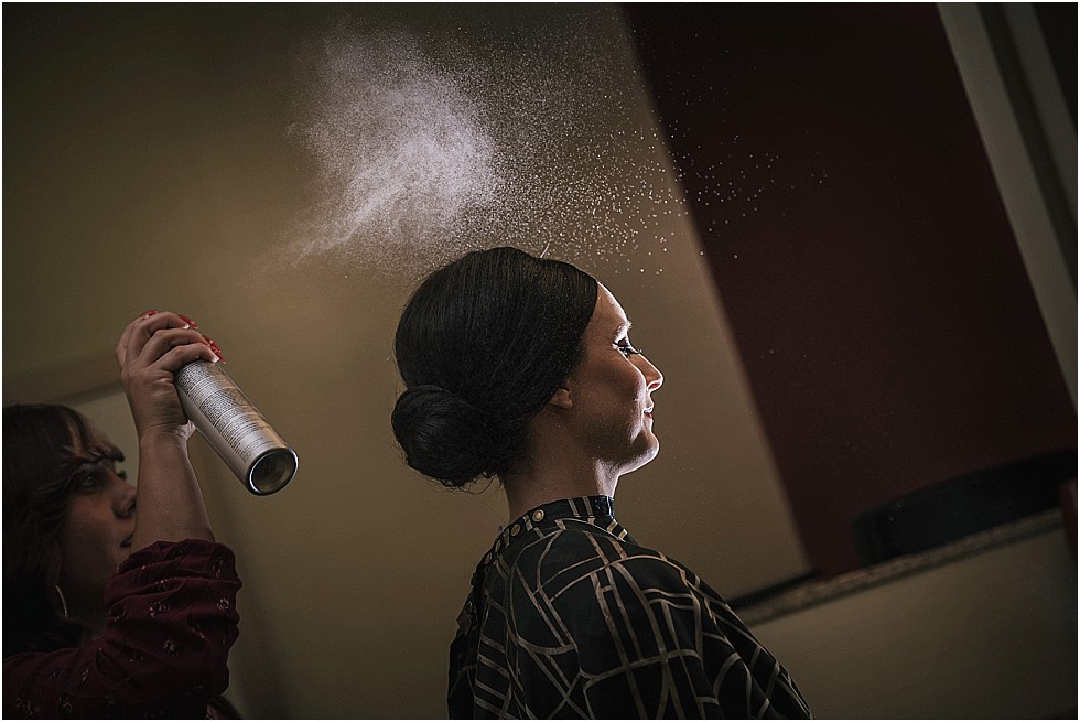 bride getting hair done with mist of hairspray