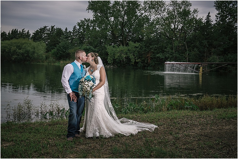 bride and groom kiss in front of pond